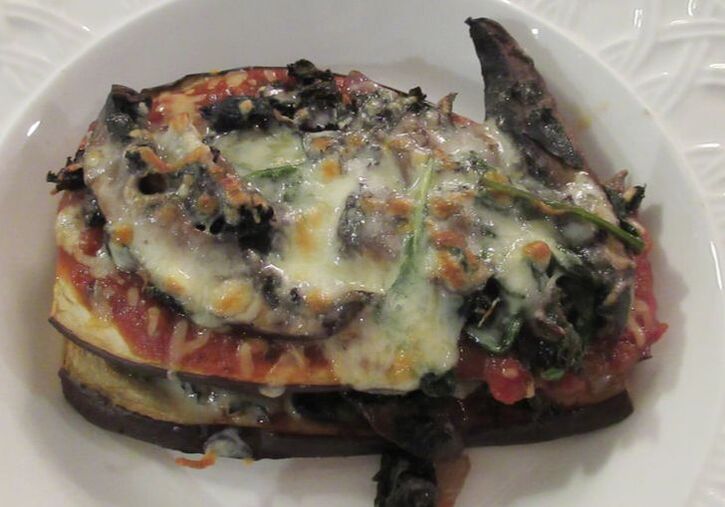 Beautifully browned eggplant strata with melted cheese oozing from layers of eggplant. Served in a whte bowl.