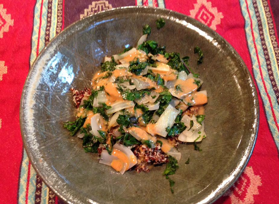 A combination of quinoa and warm kale topped with tahini sauce served in a large handmade bowl. The bowl rests on a southwest influenced cloth.