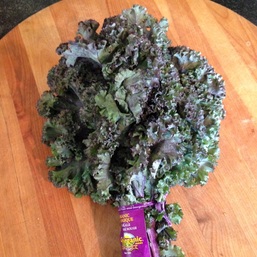 A bunch of kale resting on a round wooden cutting board.