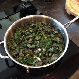 Kale sauteeing in a large stainless steel frying pan on the stove top.