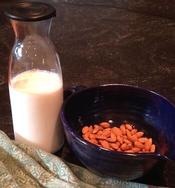 Almonds soaking in a bowl of water and a liter glass bottle of homemade almond milk.