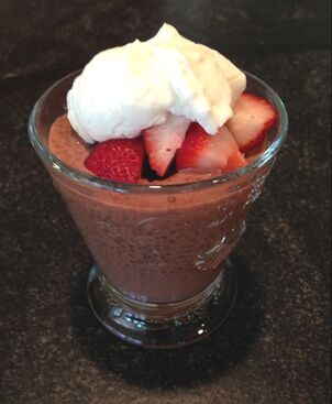 Chocolate chia seed pudding served in a fancy glass and topped with strawberries and plain yogurt.