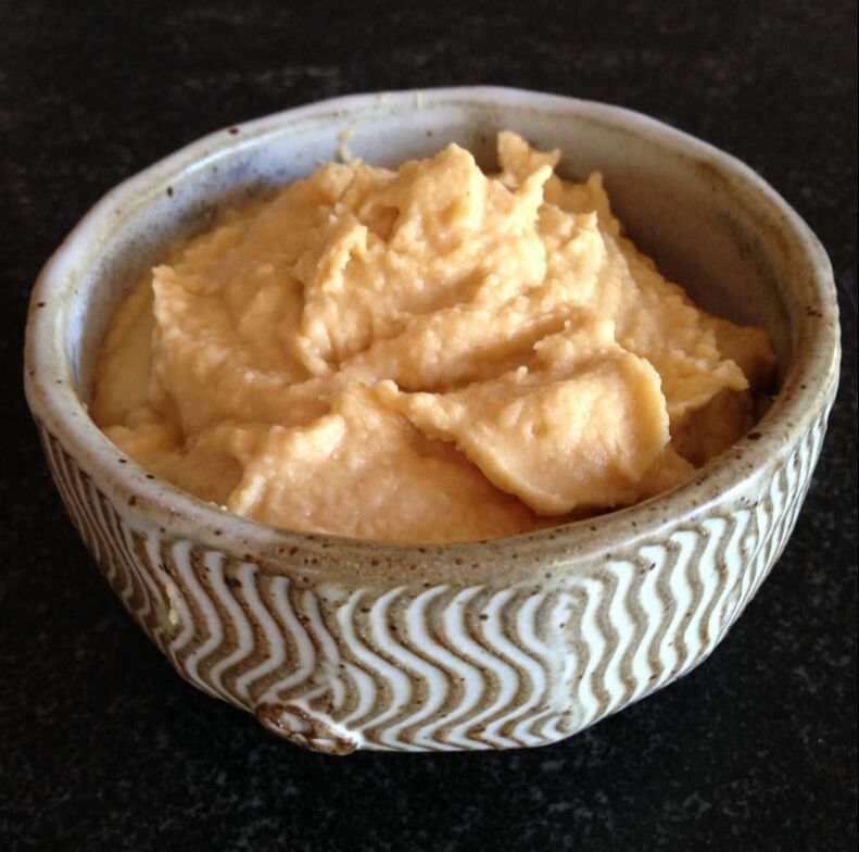 A beautiful cream colored handmade bowl filled with hummus.