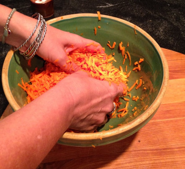 Hand mixing carrots and salt in a green bowl.