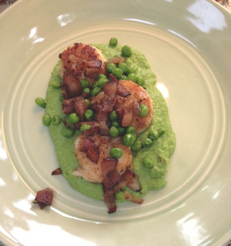 A spring green puree of garden peas topped with bacon, seared scallops and whole peas. Served on a light green porcelain plate.