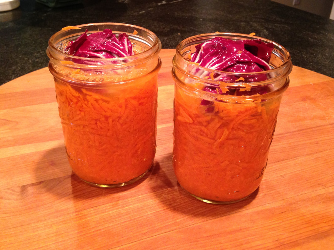 Two mason jars filled with grated carrots and salted water; topped with a piece of radachio. 