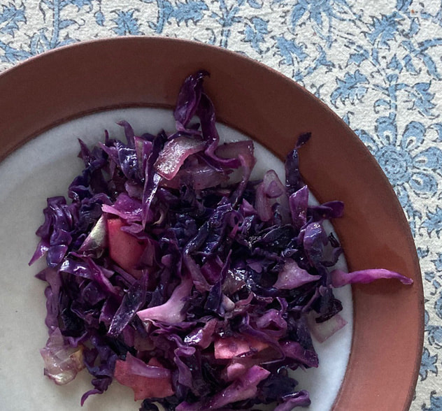 Cooked bright purple cabbage with apples and onions displayed on an olive green plate.