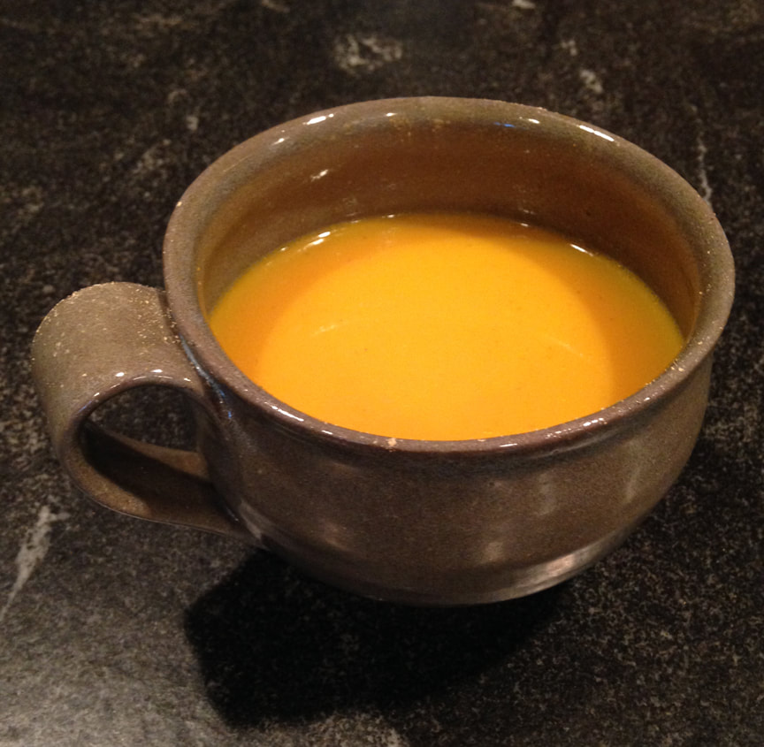 A handmade green mug filled with a bright yellow turmeric ginger tea. The mug is sitting on a black granite countertop.